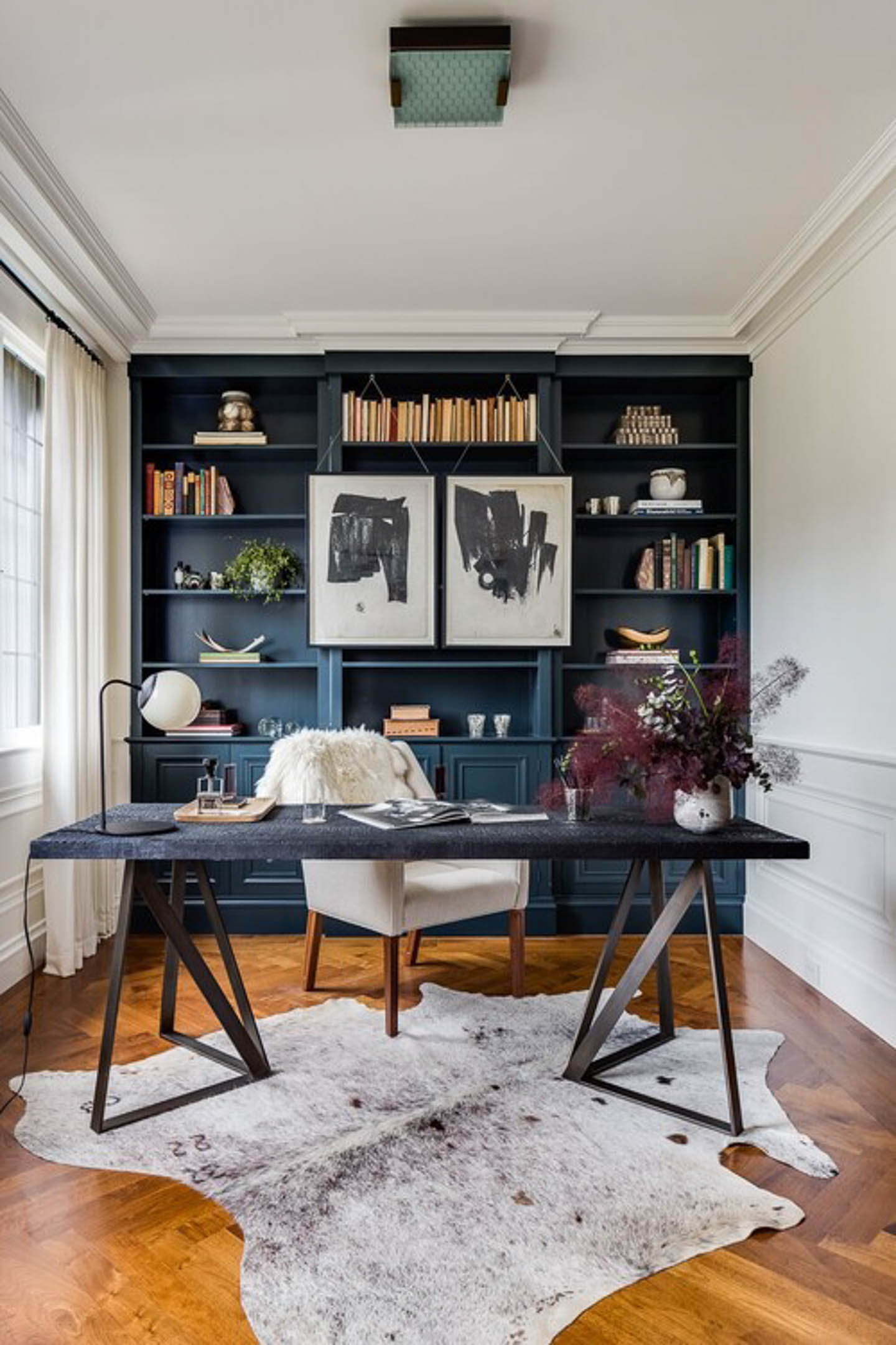 Small home office with dark blue shelves across one end, a black desk in front and walls painted white