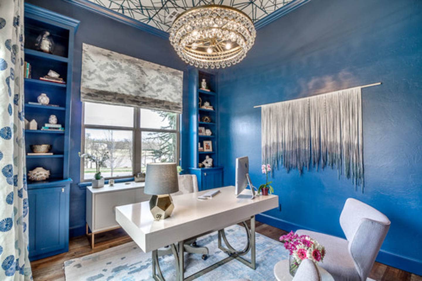 Home office painted in gloss blue paint with a white desk and chair, and blue and white ceiling, curtains and rug