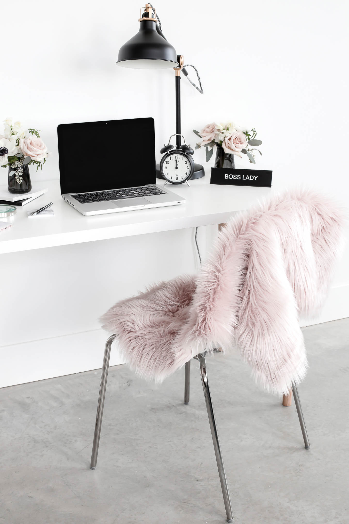 Pink furry blanket over a chair in front of a white desk with a laptop and lamp