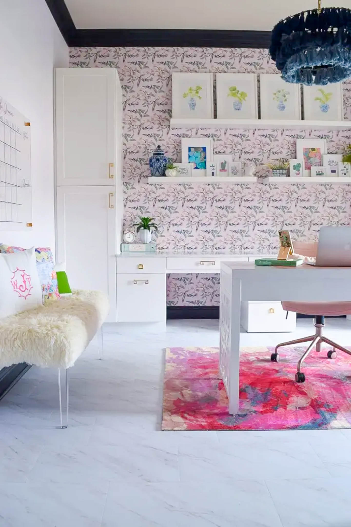 Feminine home office with pink and blue wallpaper, white fur bench and a blue tassel chandelier