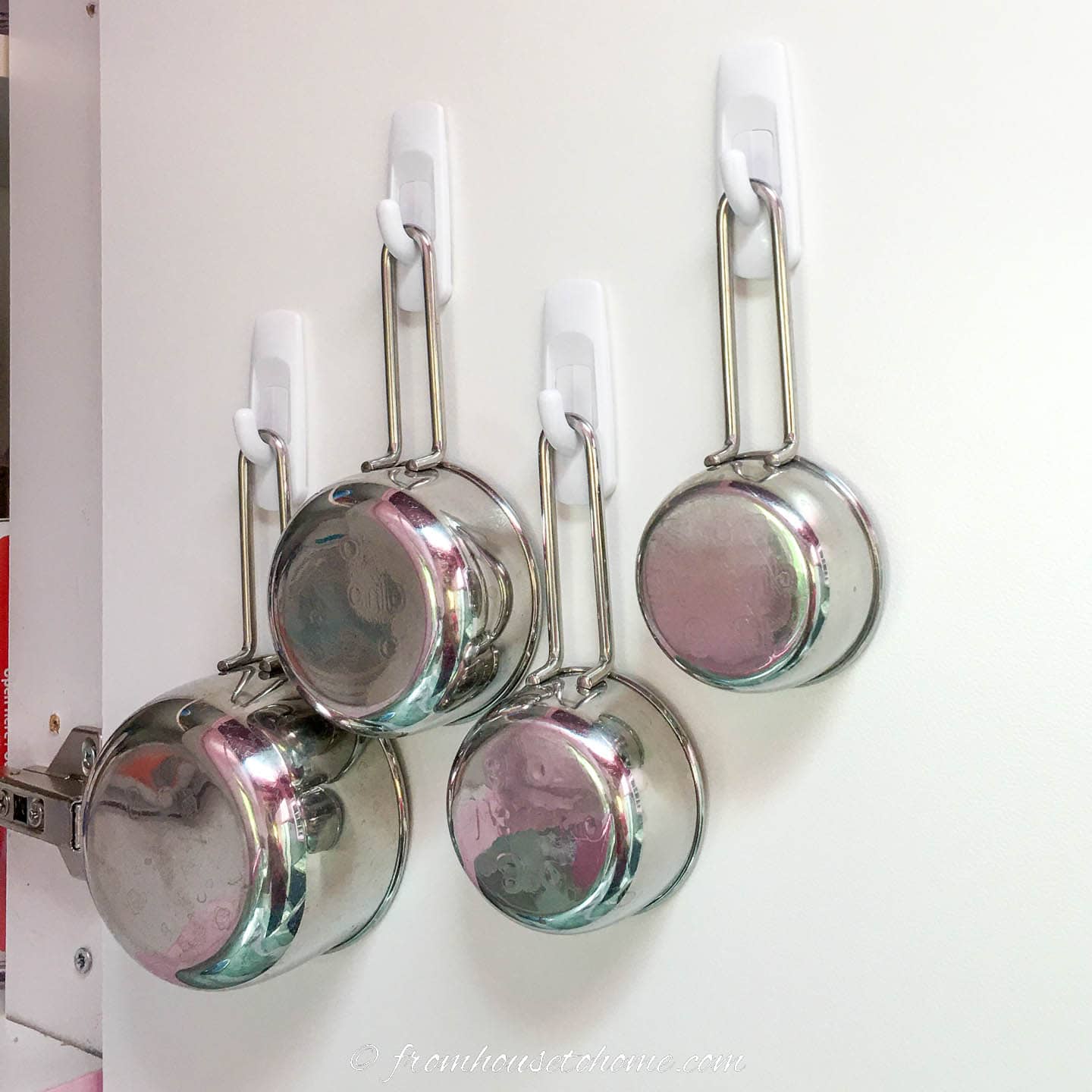 Measuring cups hung on the inside of a kitchen cabinet door with Command hooks
