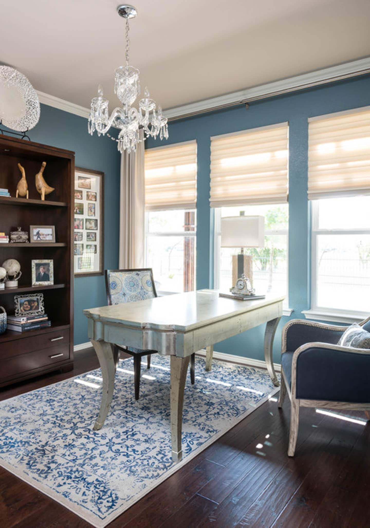 Small home office with teal walls, a silver desk, and a blue and white patterned chair and area rug