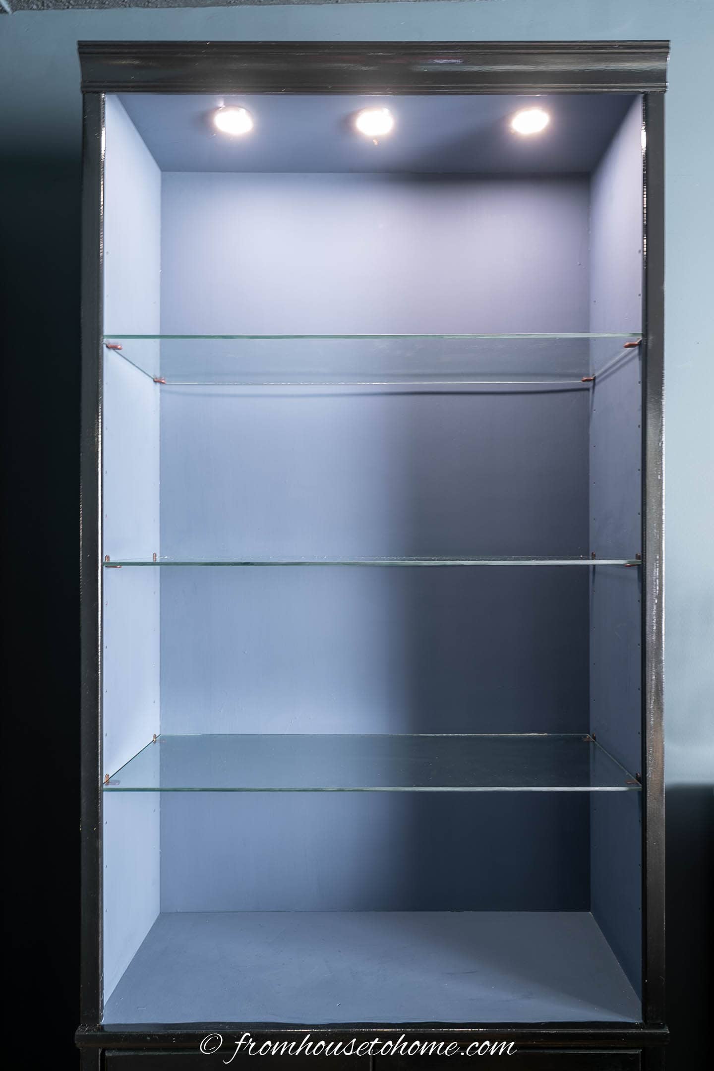 Puck lighting installed at the top of a bookcase with glass shelves