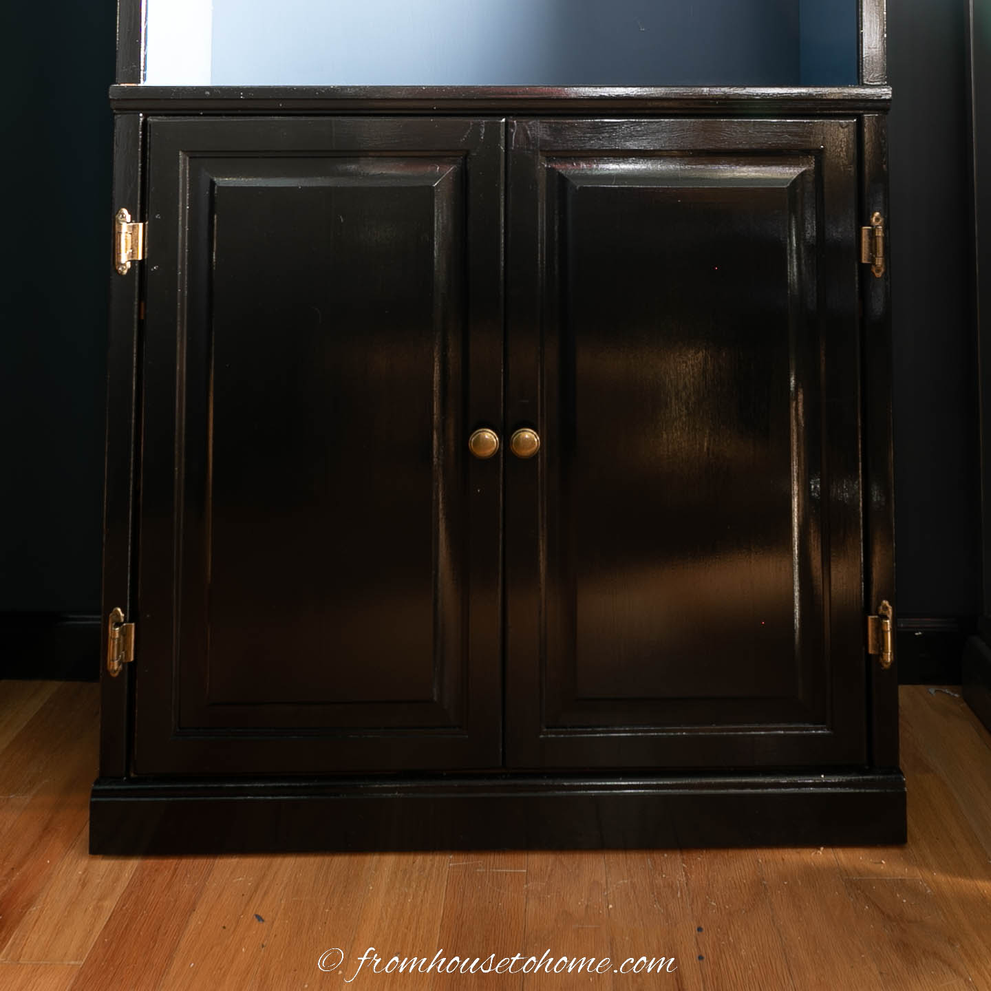Cabinet doors at the bottom of the bookshelf painted in gloss black paint with brass hardware