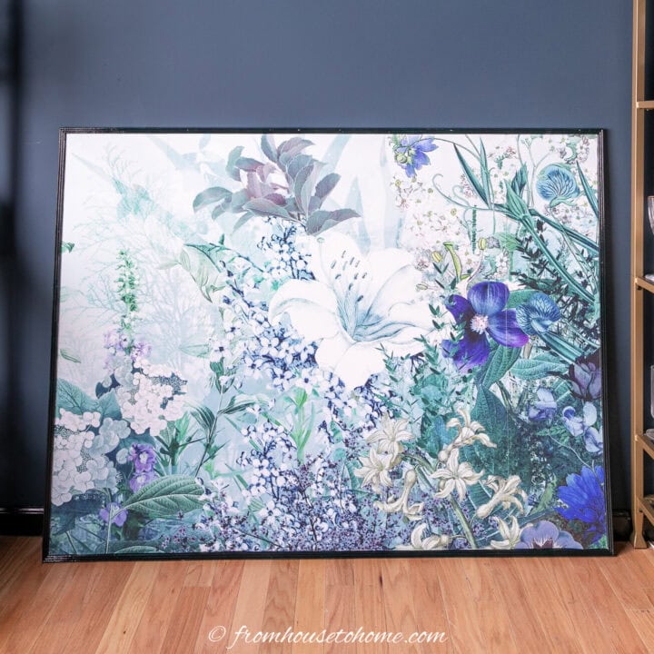 Framed artwork featuring various illustrated flowers and plants in shades of blue, purple, and green against a light background.