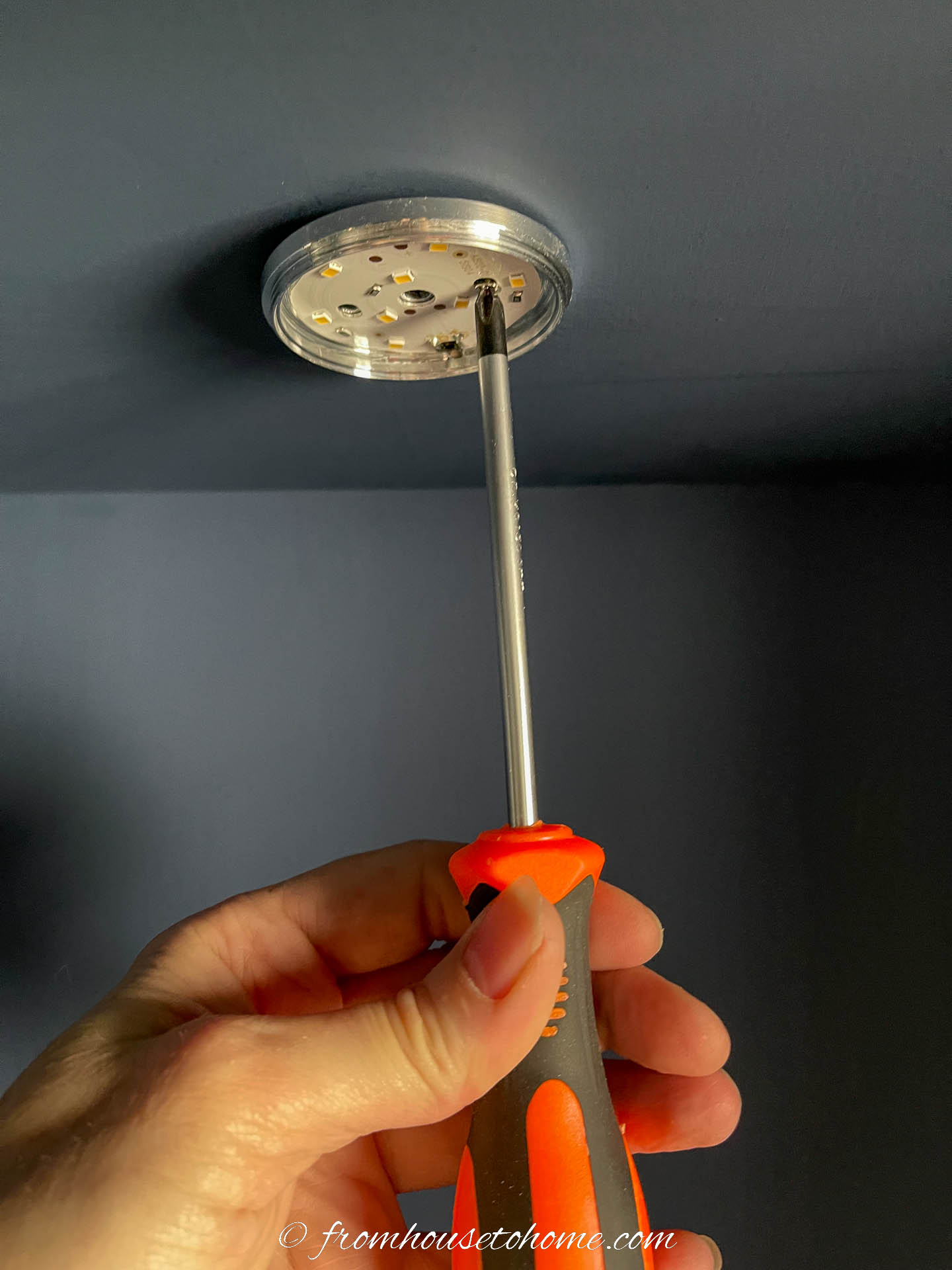 Puck lights being attached under a shelf with screws