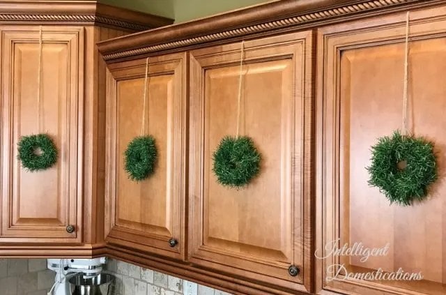 Mini Christmas wreaths hung from kitchen cabinet doors