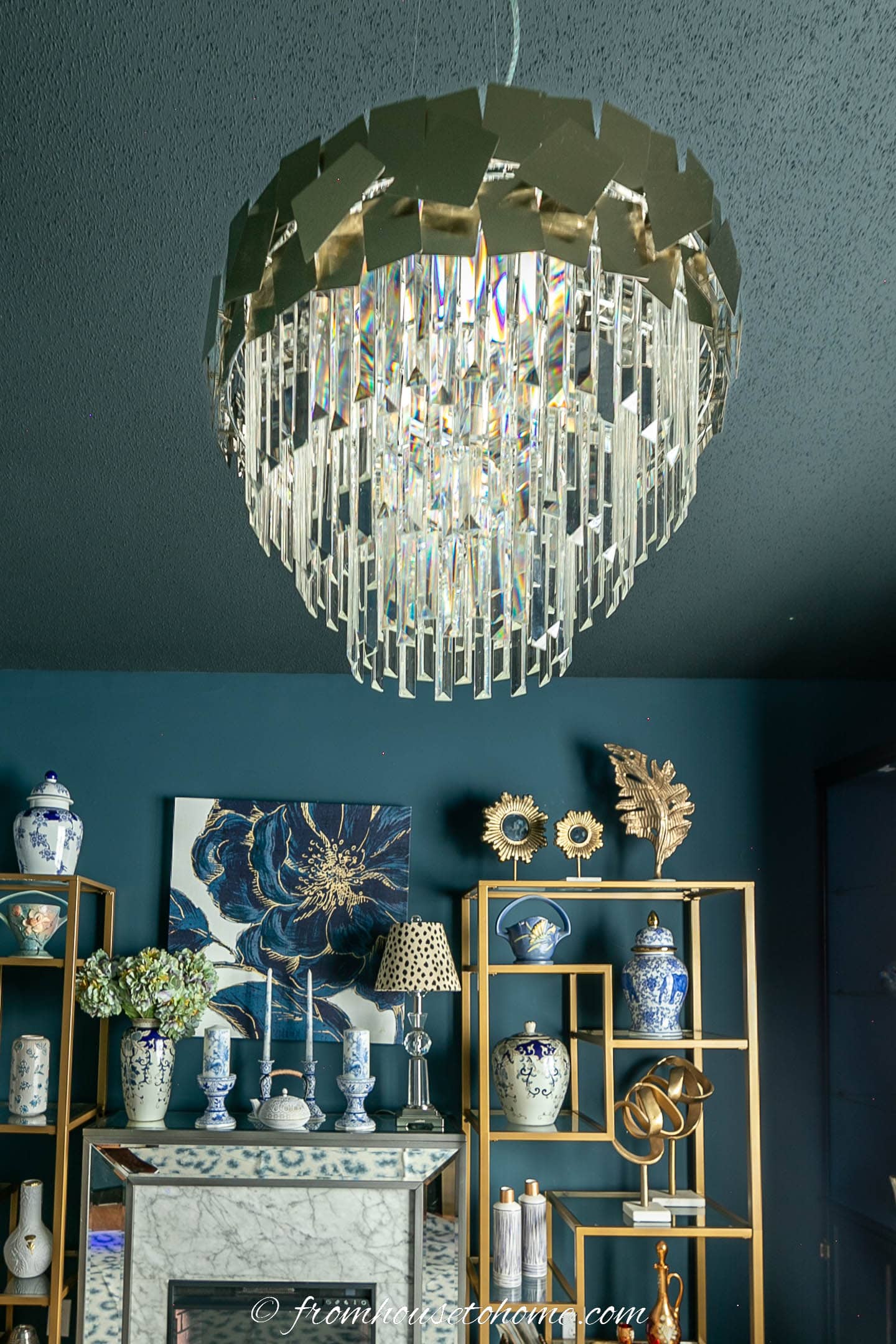 A large gold and crystal chandelier in front of a fireplace and a gold shelf