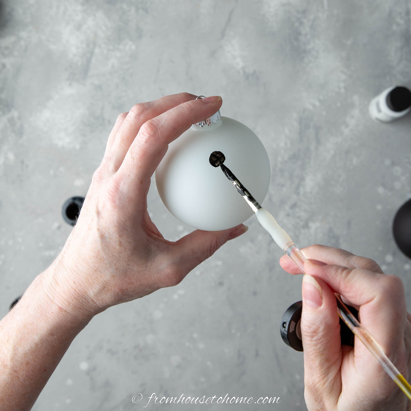 A black polka dot being painted on a white ball ornament