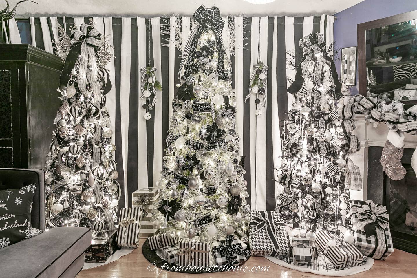 Three black and white Christmas trees with black and white wrapped presents in front of a wall of black and white striped curtains