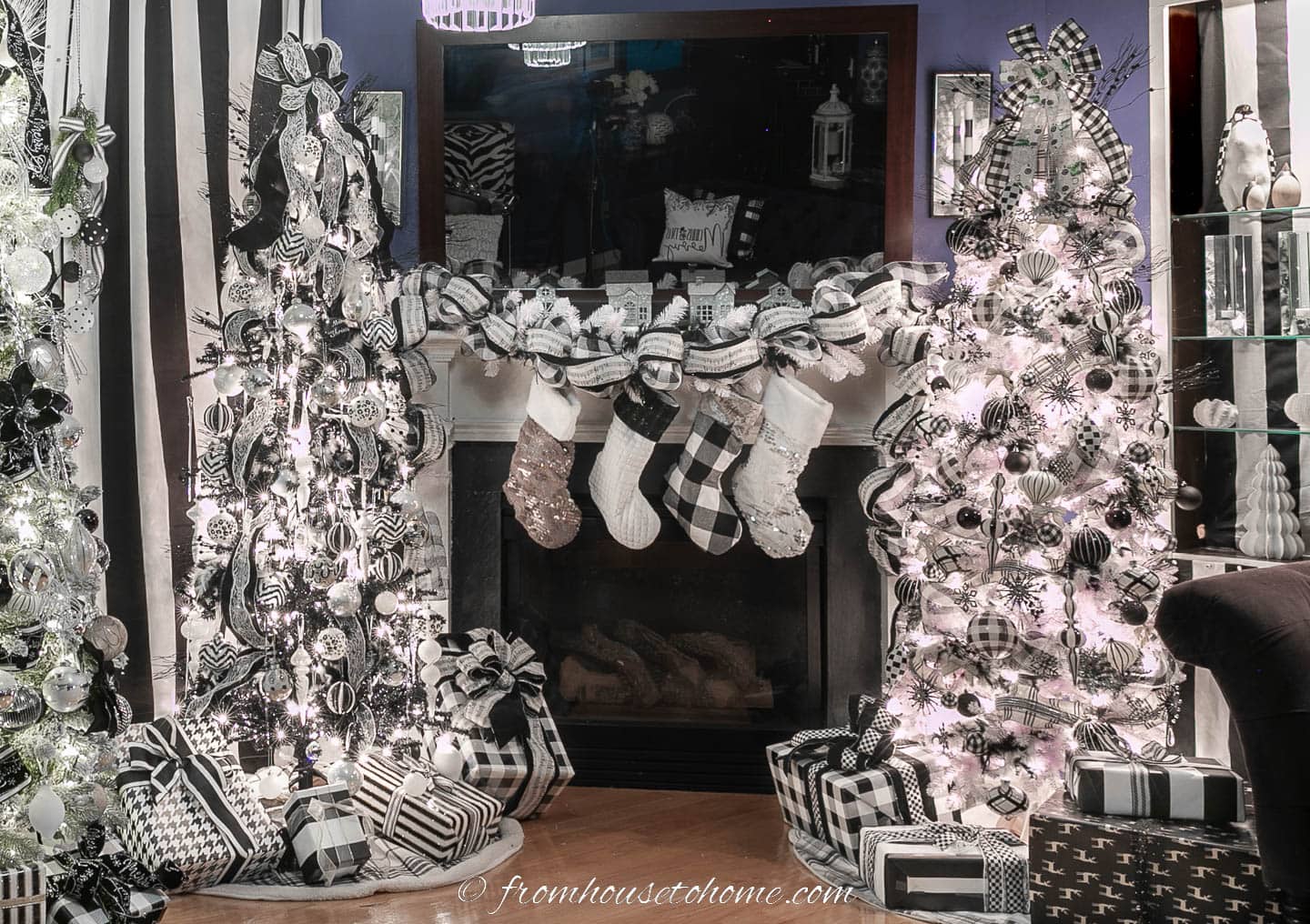 Two black and white Christmas trees on either side of a fireplace with a black and white garland and stockings and presents under the trees