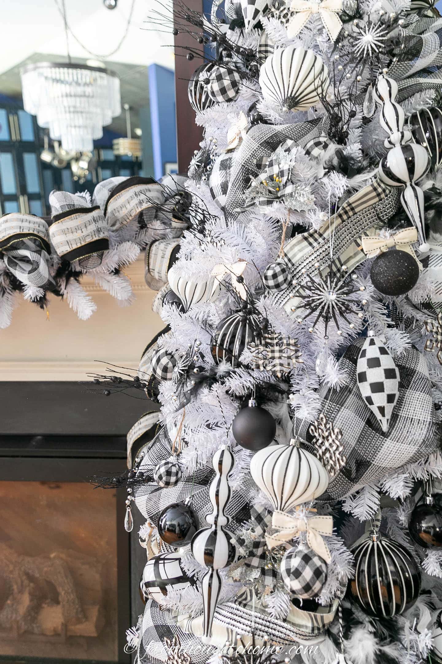 A white Christmas tree with black and white plaid ornaments in front of a fireplace mantel with a black and white garland