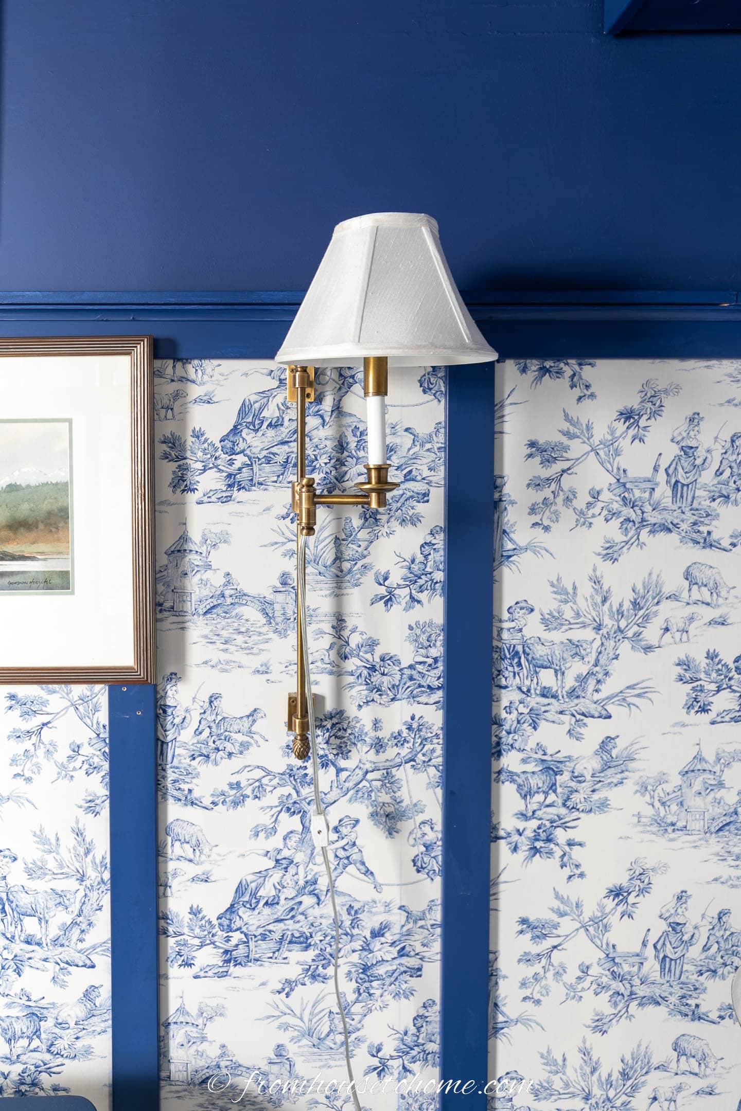 Gold and white sconce hung on a blue and white toile wall
