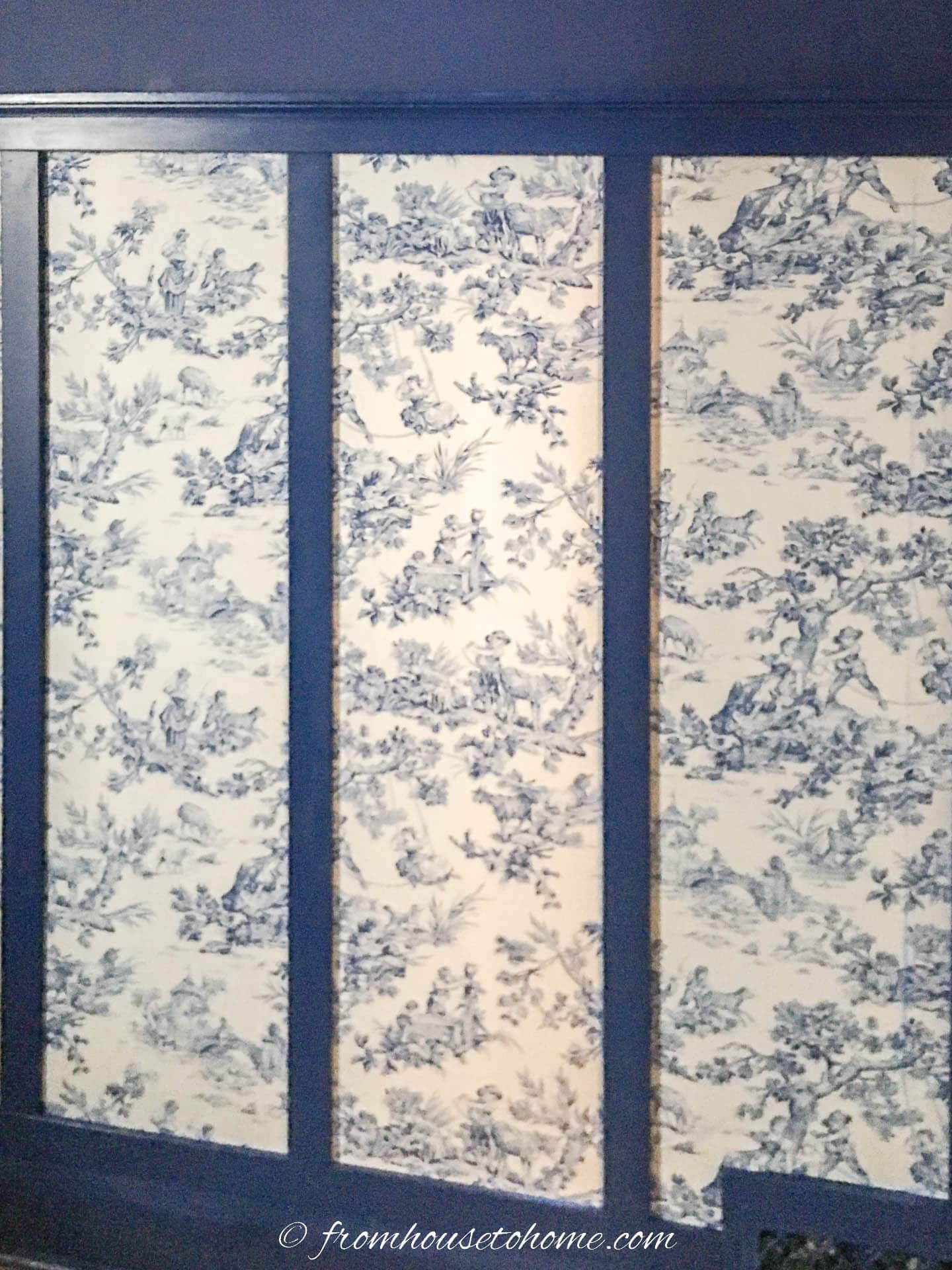A wall with blue board and batten trim and blue and white toile fabric in between 