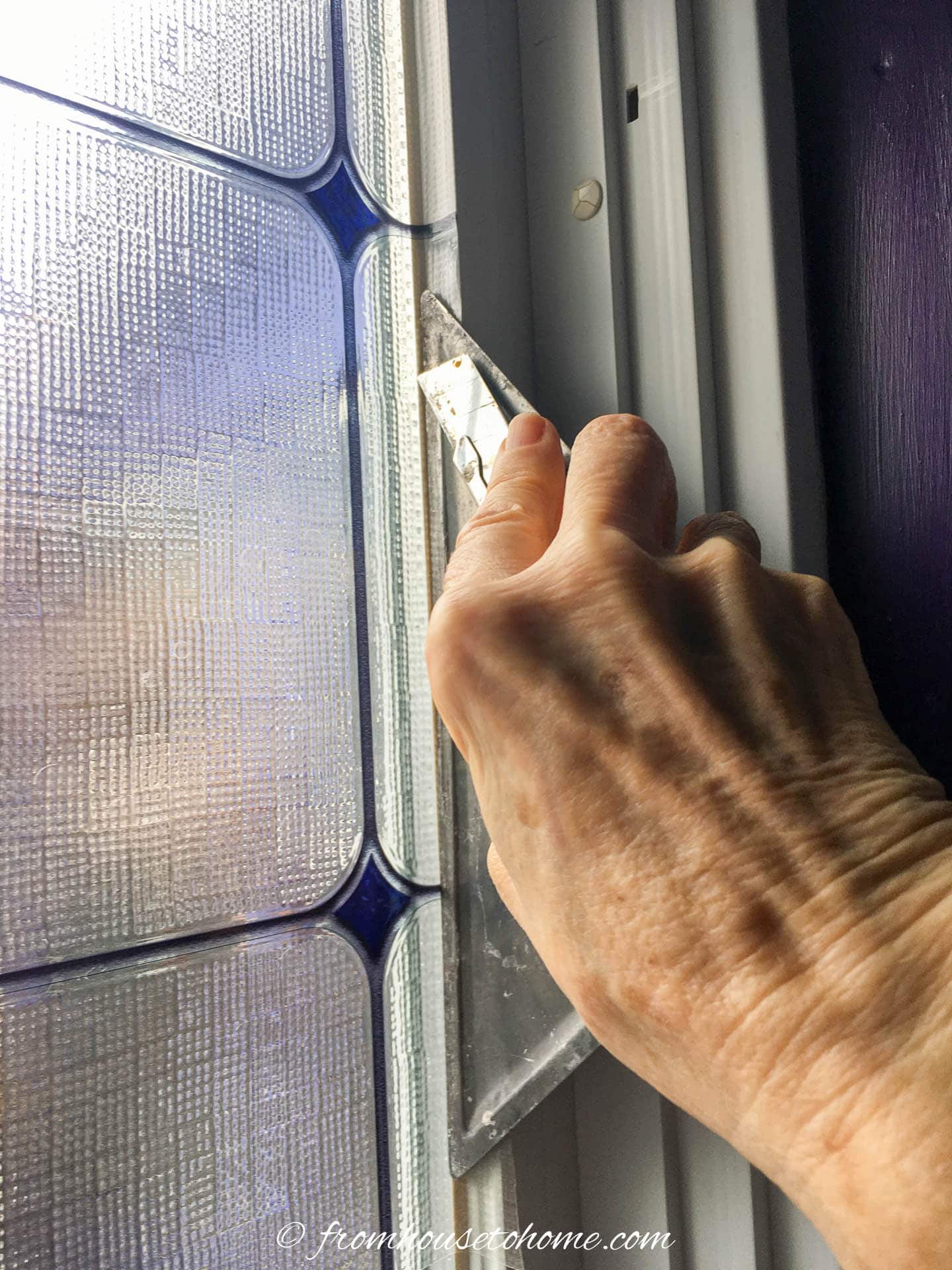 Utility knife cutting the adhesive window film along the edge of the window