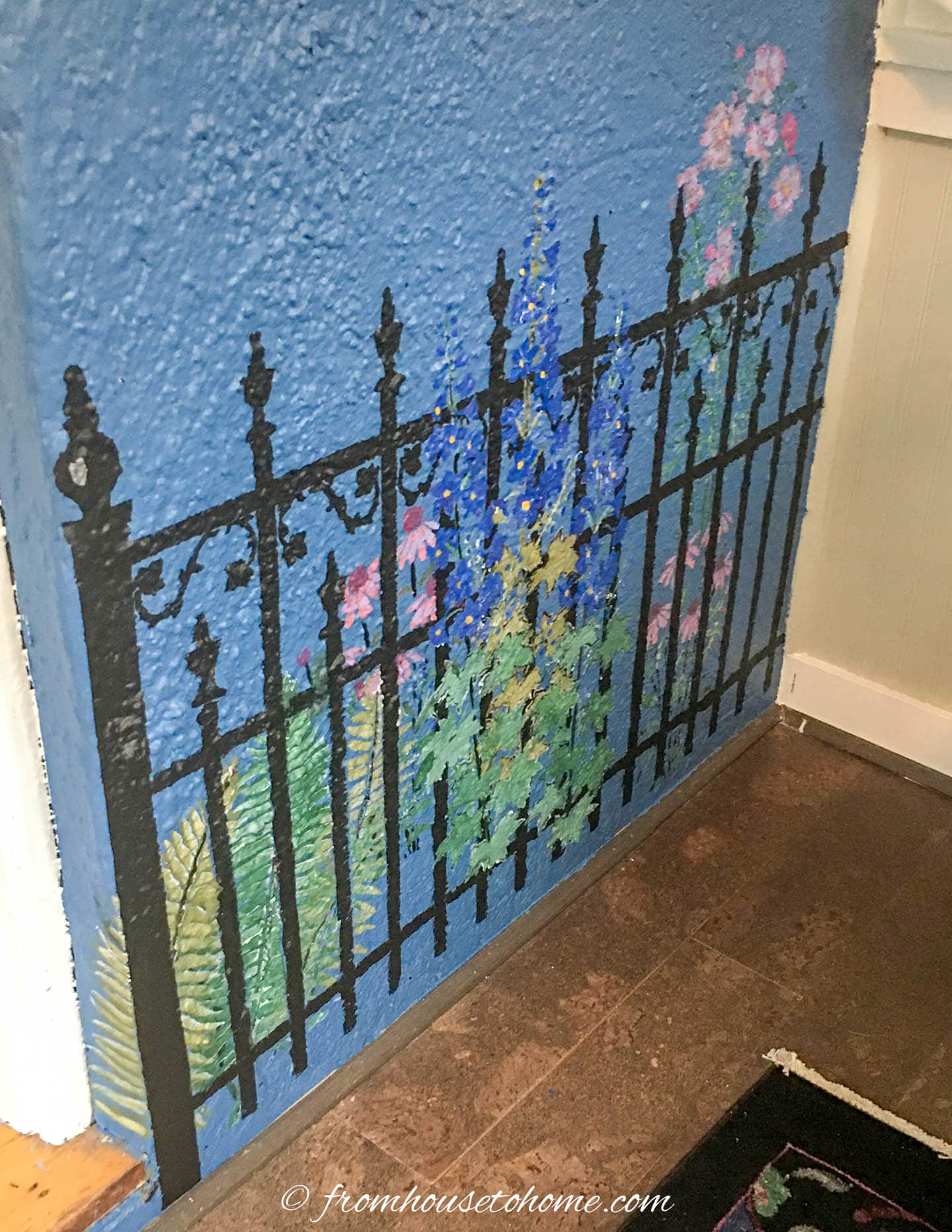 Stencil of a wrought iron fence with a garden behind it on a blue wall