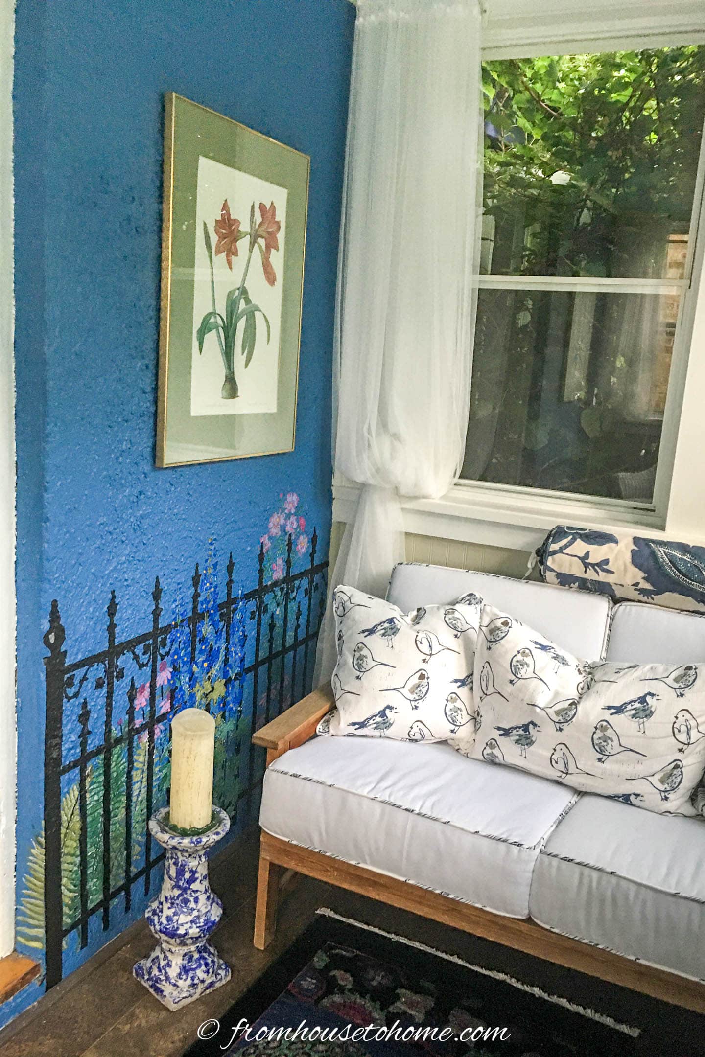 Blue and white front porch with a pine loveseat sofa, white curtains, and a blue wall with a stenciled garden