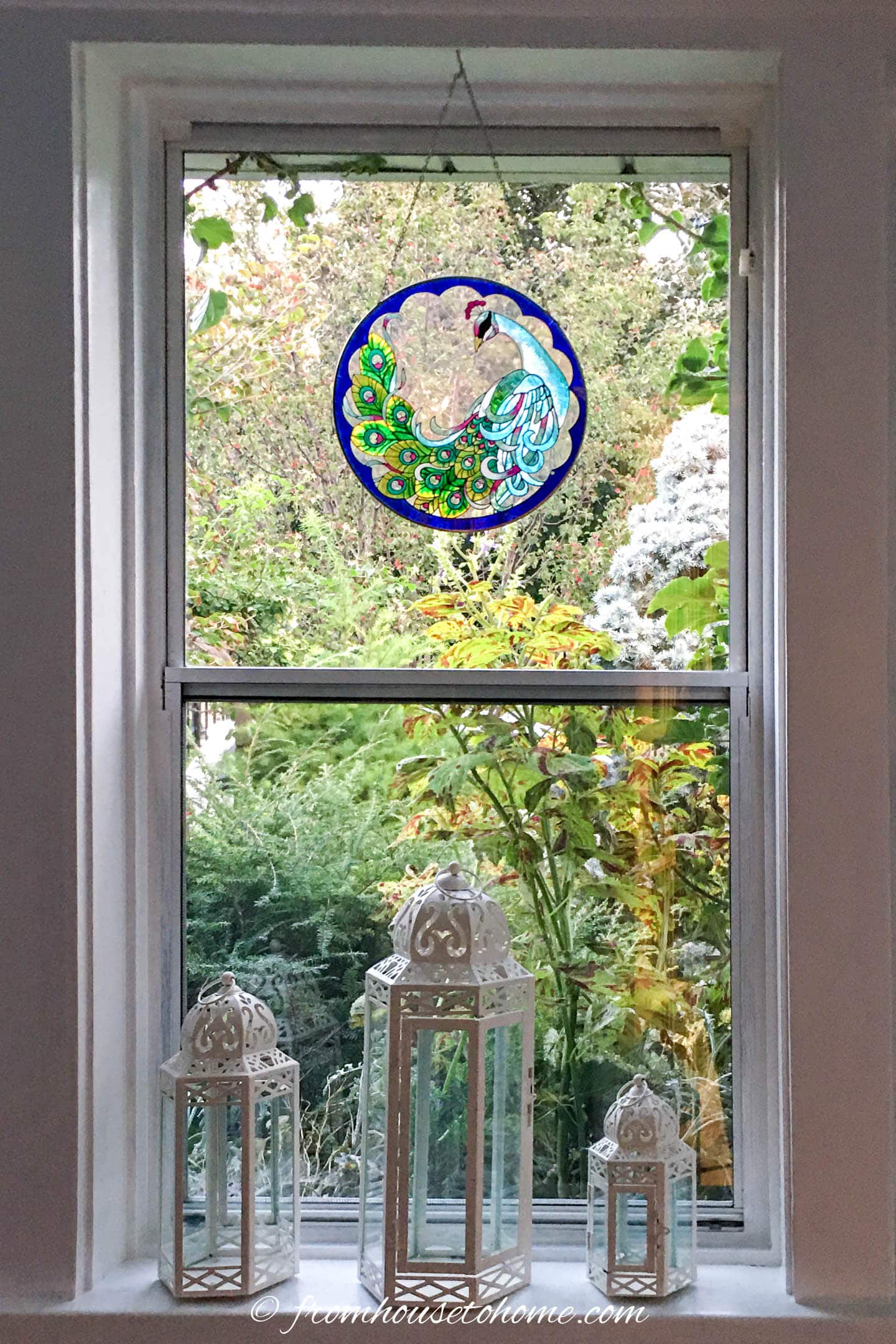 A window with a peacock sun catcher and white lanterns