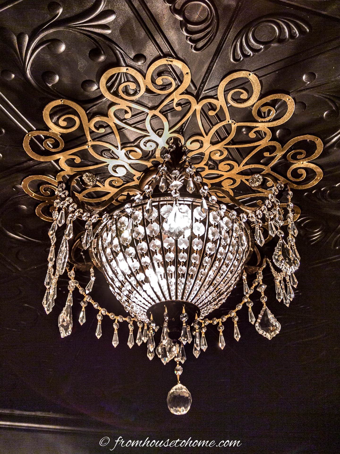 Chandelier hung on a black ceiling with a gold DIY lace ceiling medallion around it
