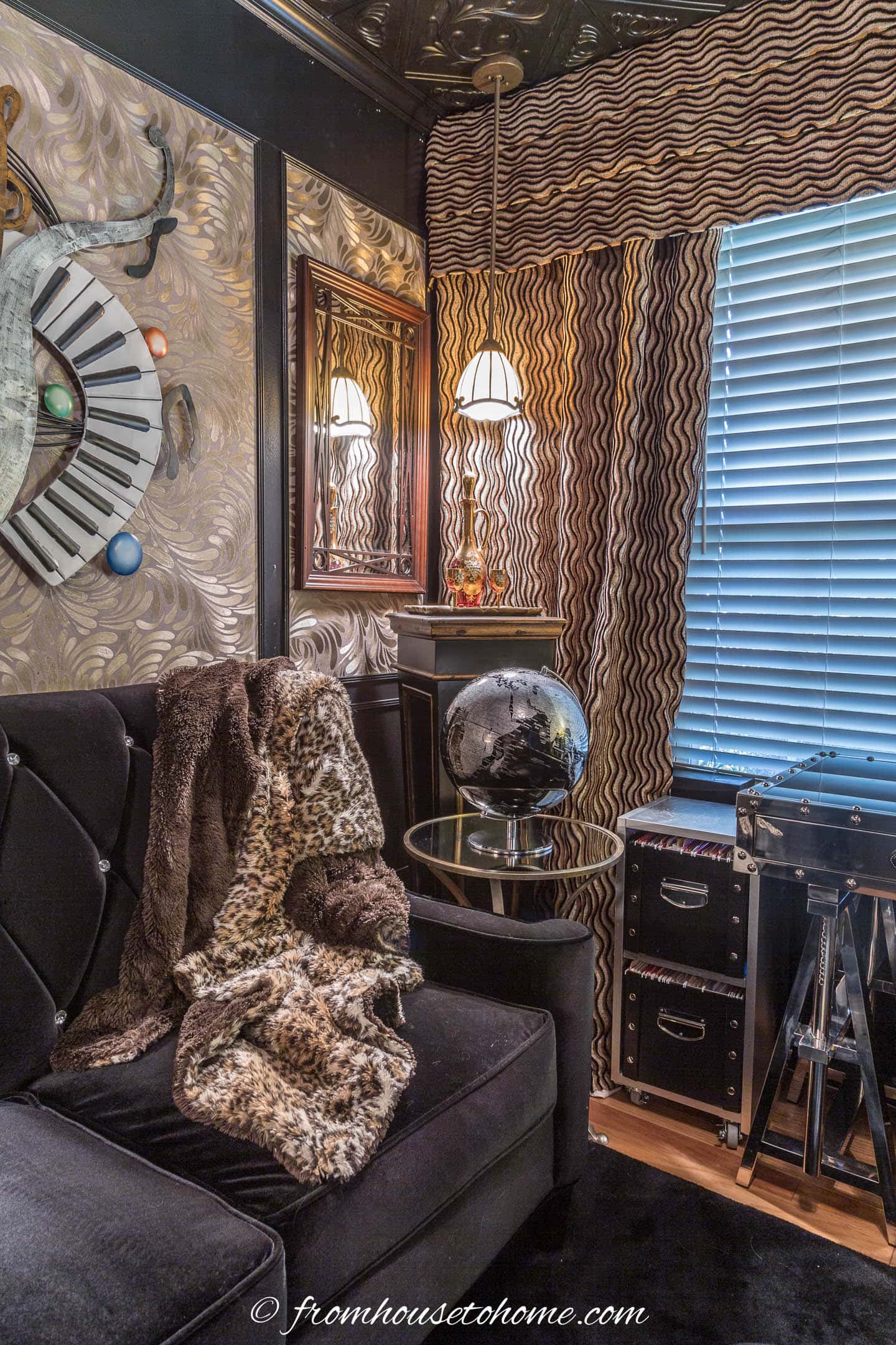 A corner of the home office library with a black velvet sofa, leopard throw, black globe and gold wine glass set