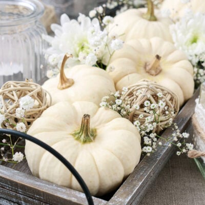 A wooden tray featuring fall home decor ideas with white pumpkins and flowers.