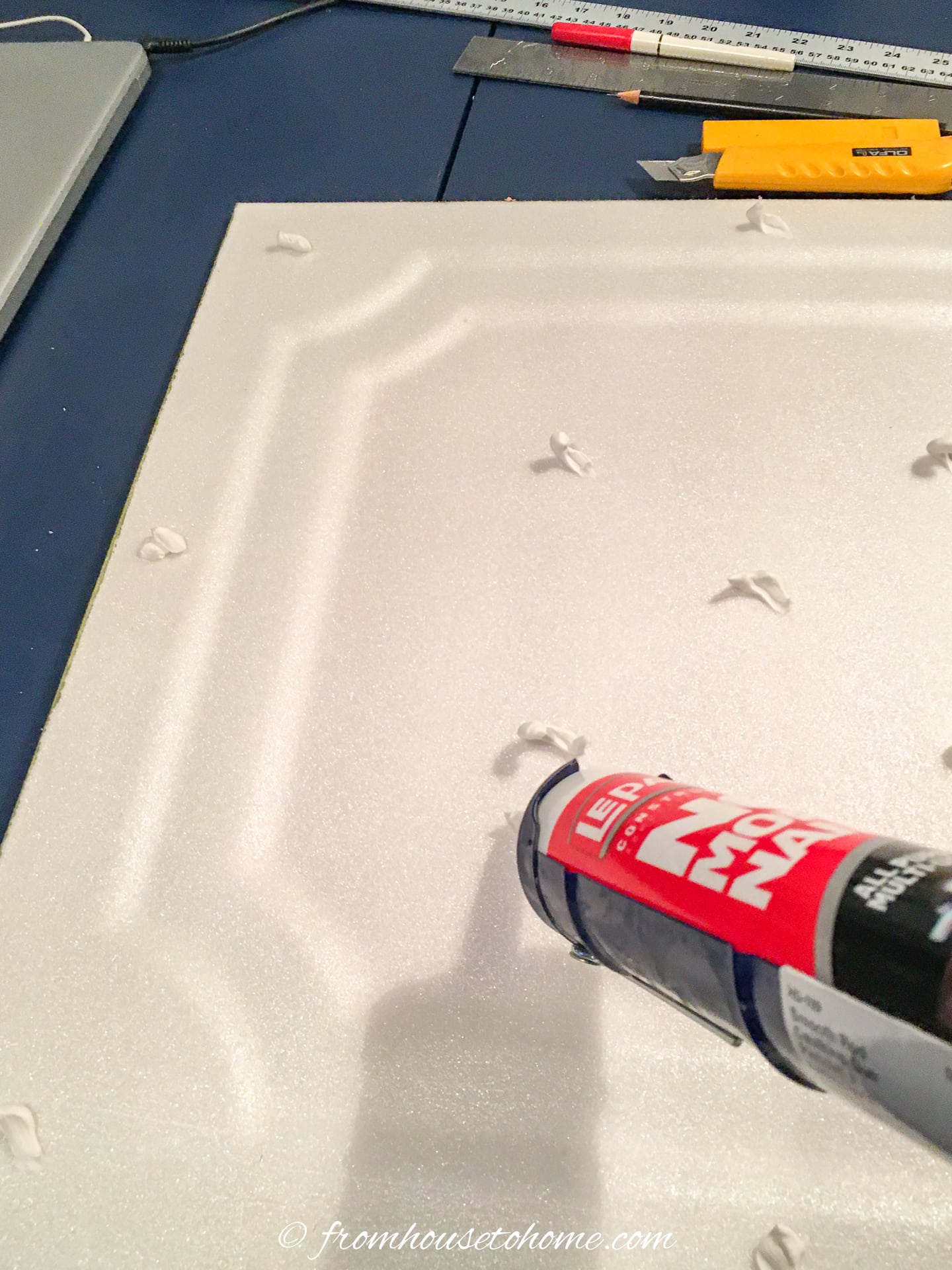 Liquid nails being applied to the back of a faux tin ceiling tile