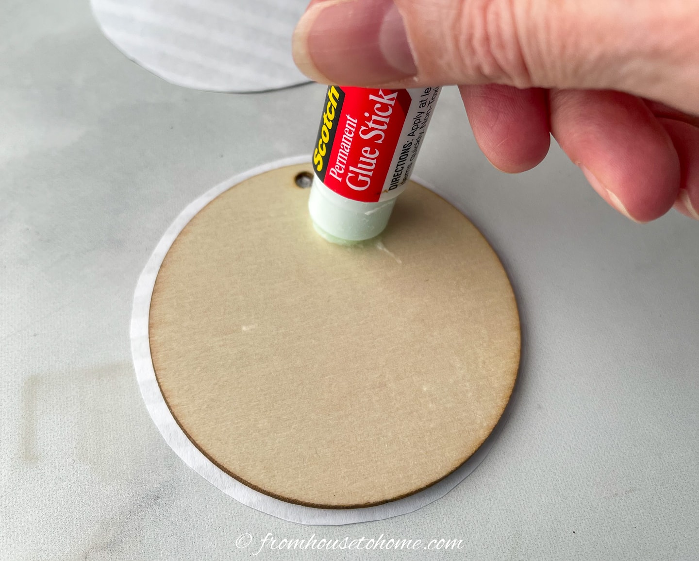 Glue being applied to the back of a round wood disc ornament