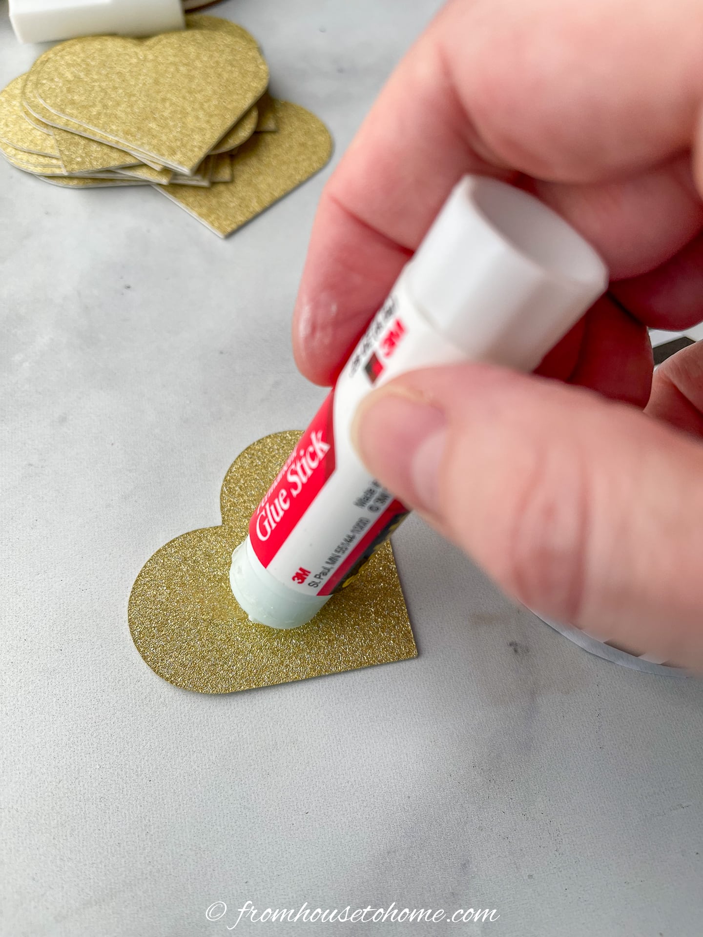A person is using a glue stick to put glue on a gold heart