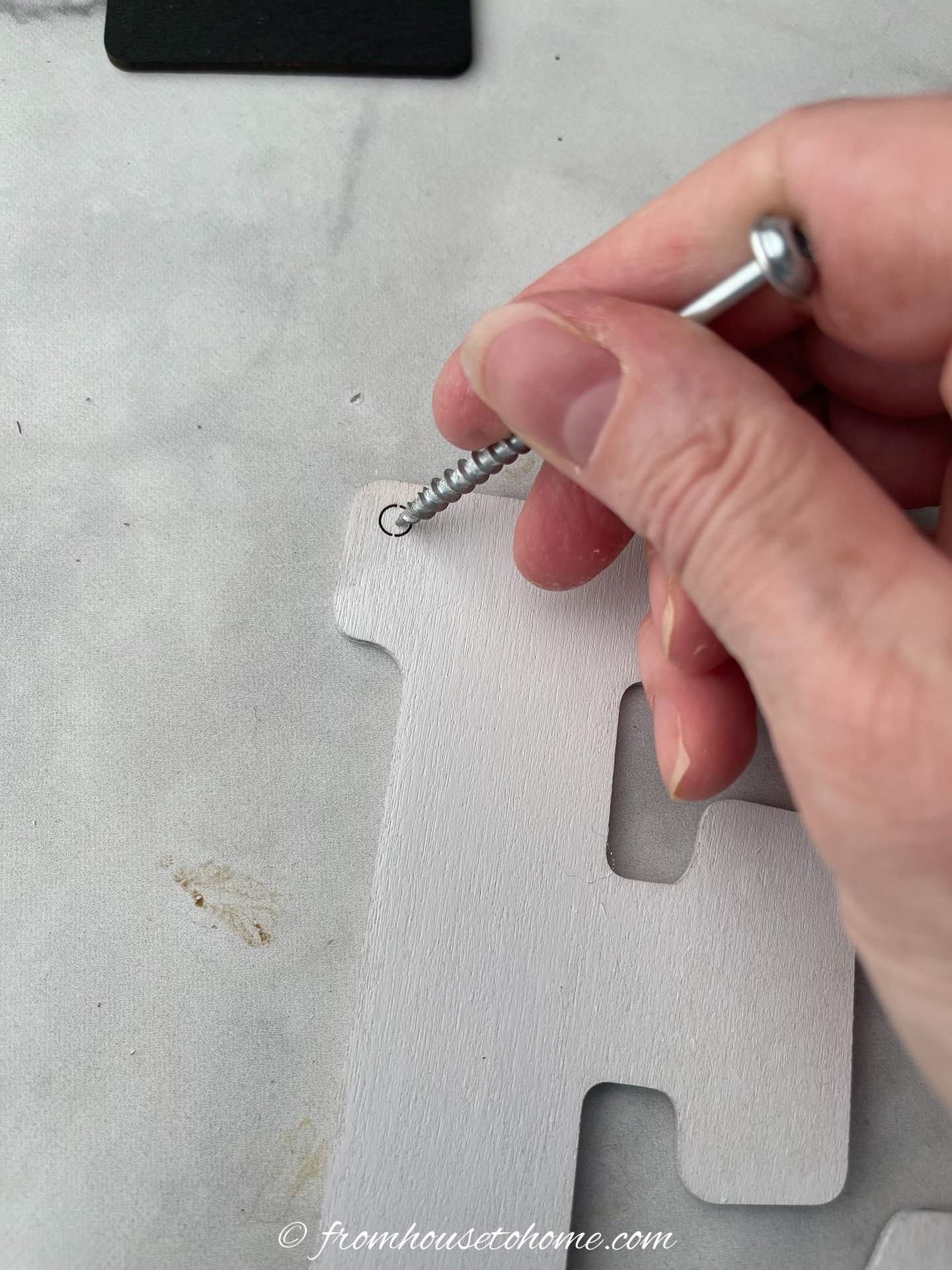 A screw pushing a plug out of the hole in a wood letter