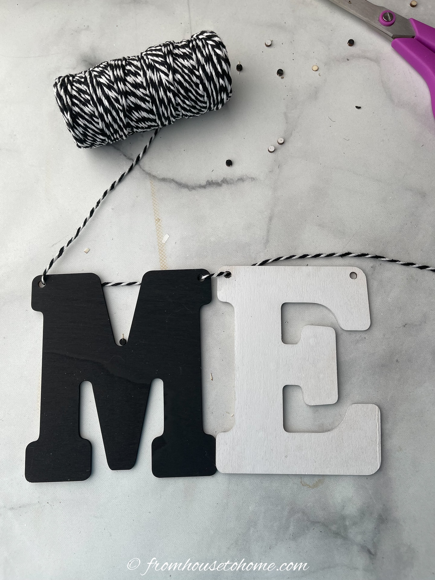 black and white string being threaded through painted wood letters