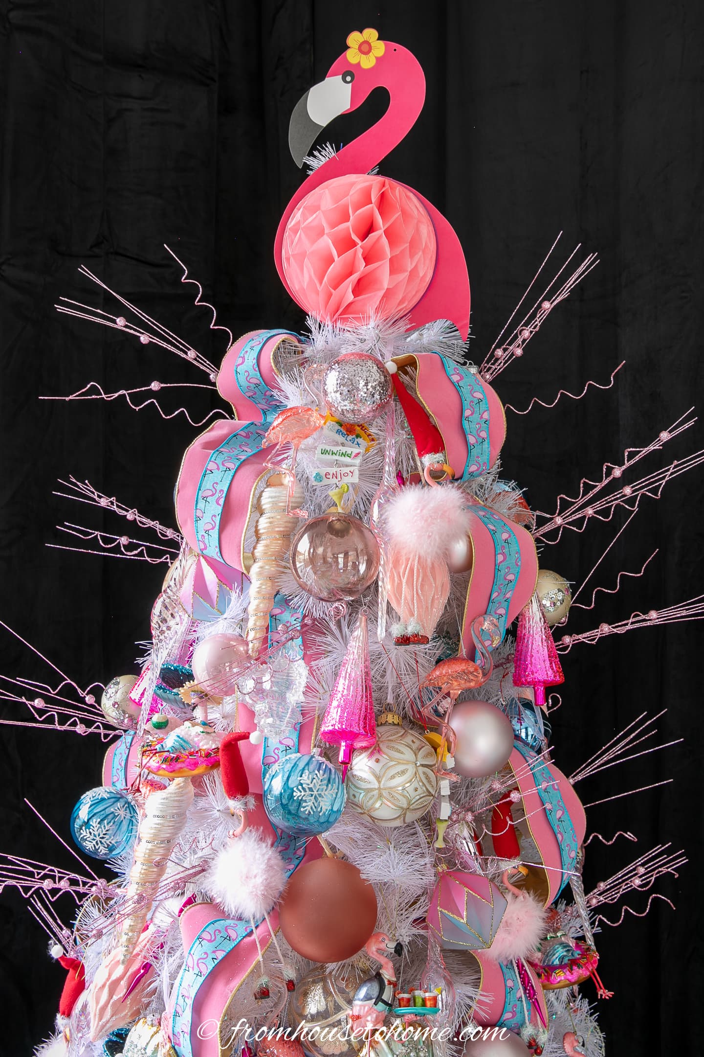 A pink flamingo tree topper and pink glitter picks at the top of a flamingo Christmas tree