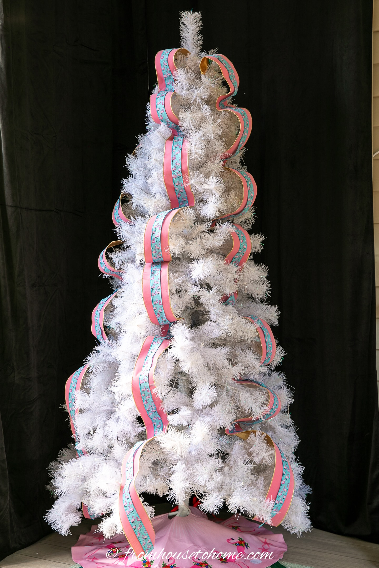 A white Christmas tree with pink and blue ribbon hung vertically