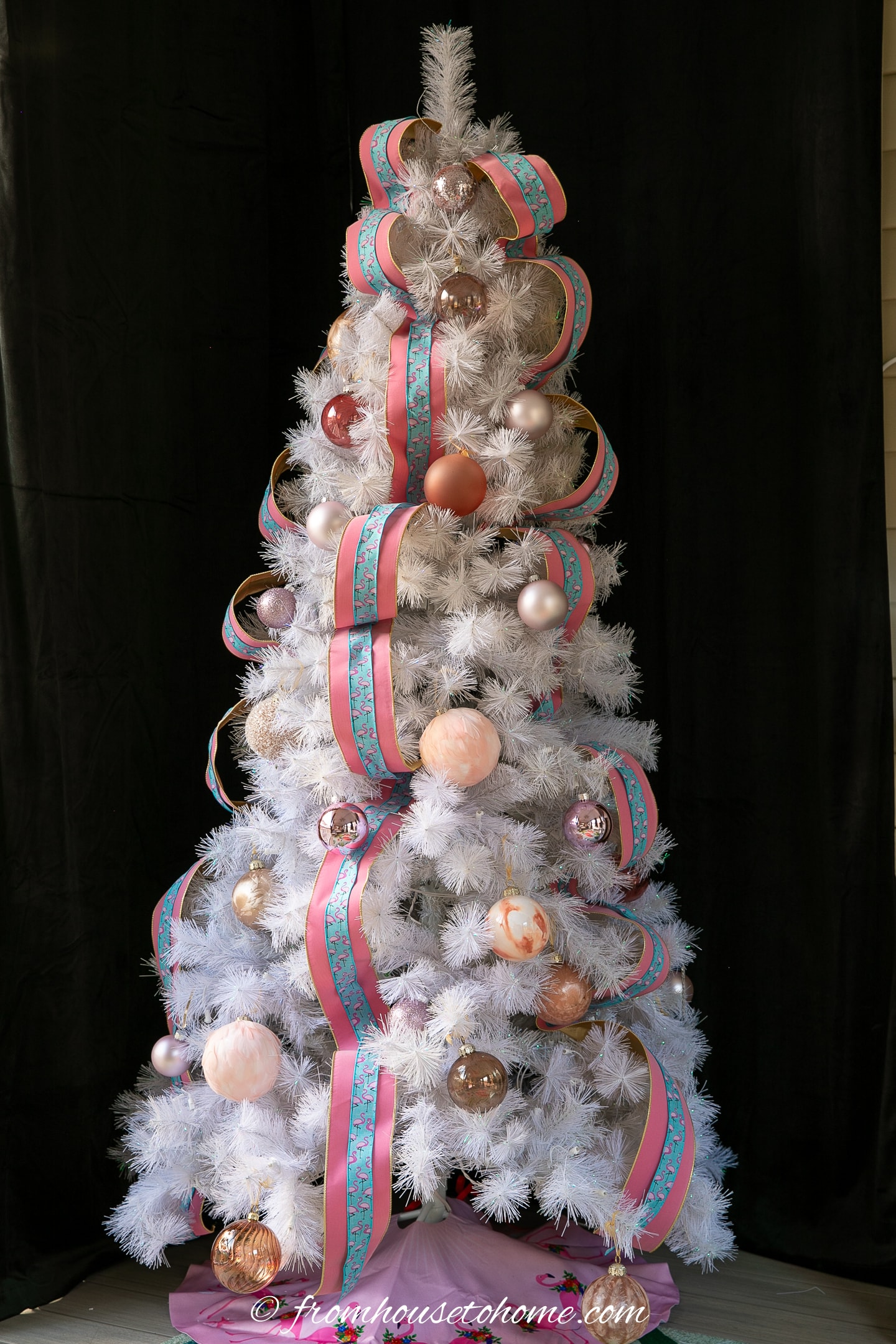 A white Christmas tree decorated with pink ornaments and pink and blue ribbons.