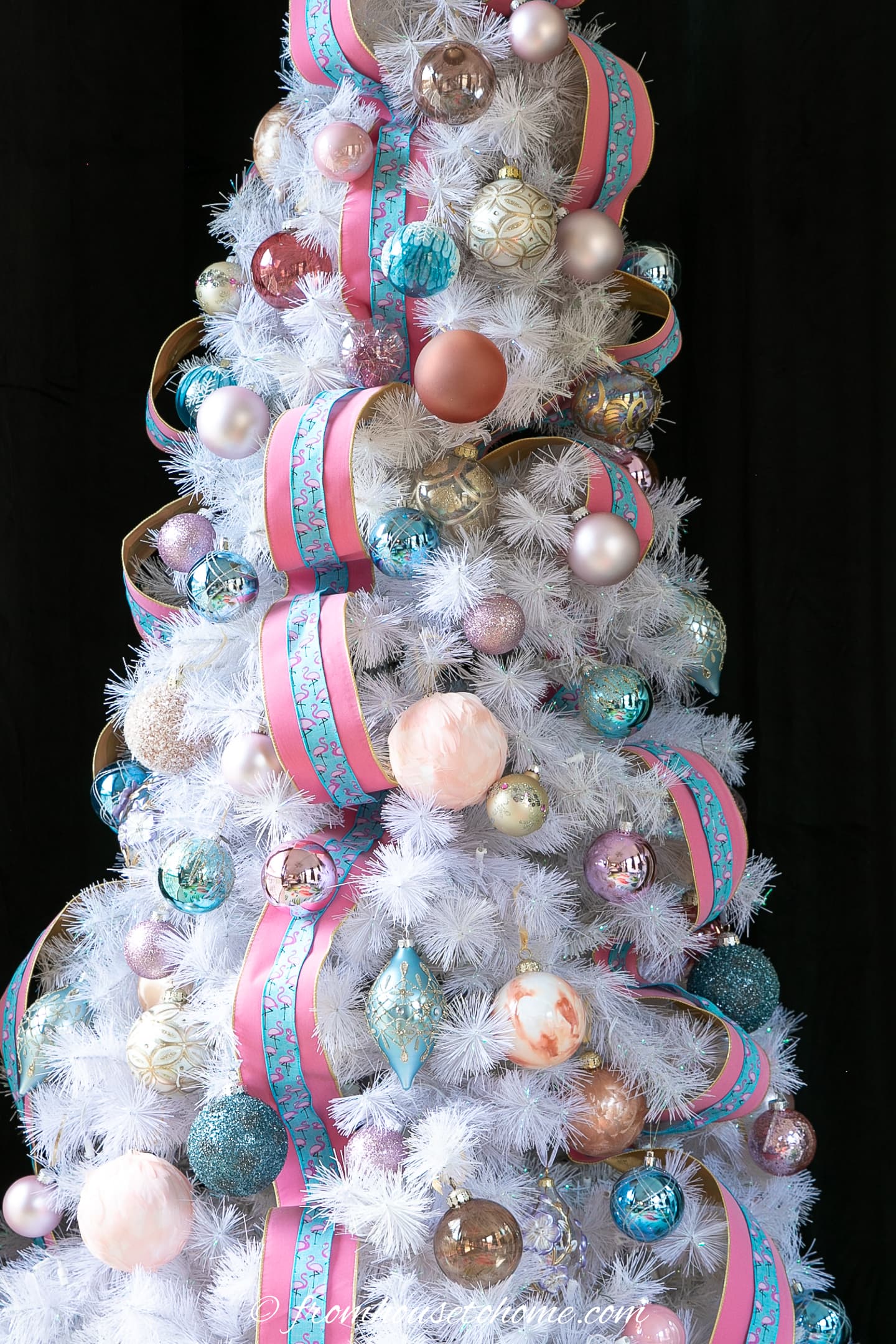 A close up of a partially decorated Christmas white tree with pink and teal ornaments