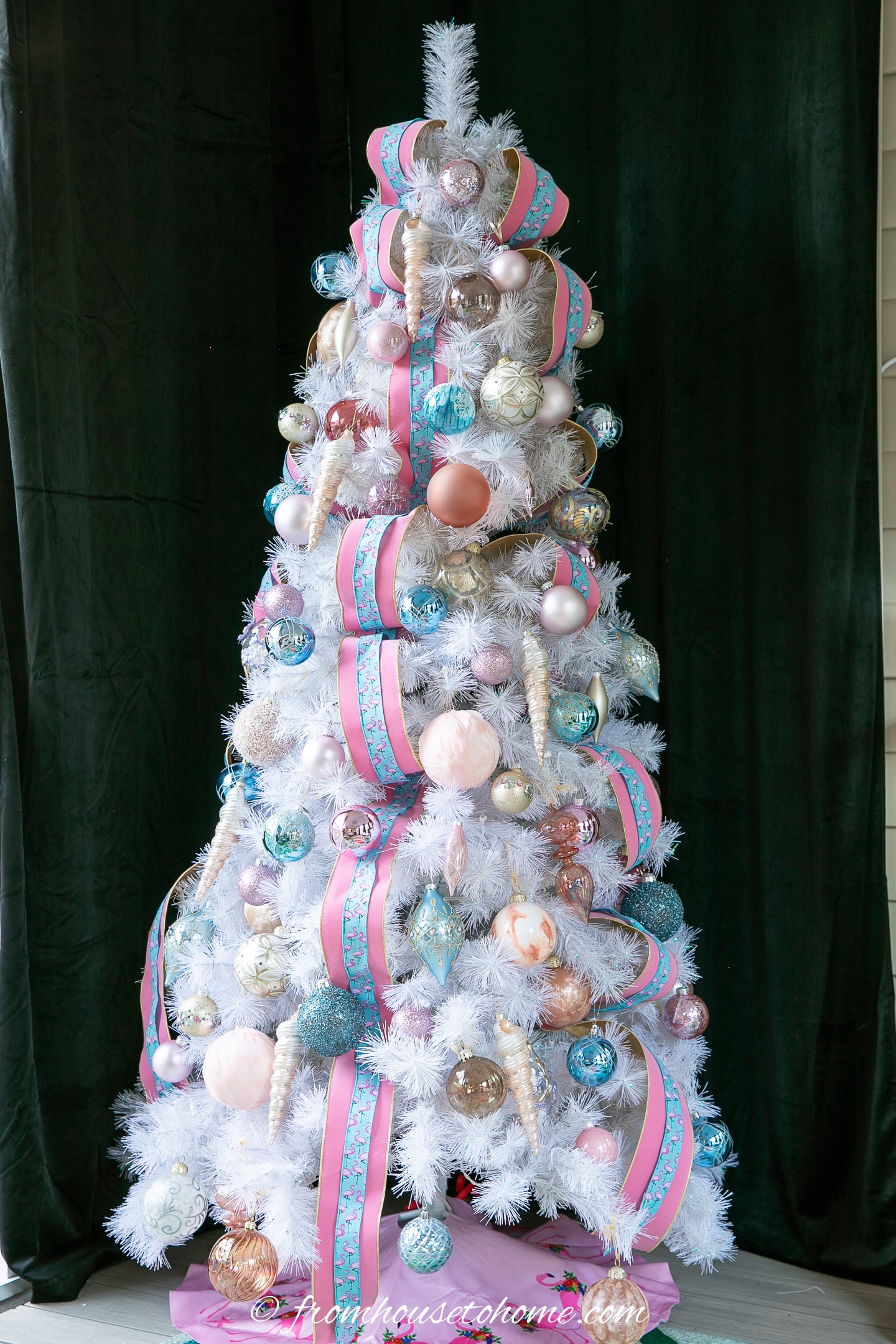 A white Christmas tree decorated with gold, teal and pink ornaments and ribbon.