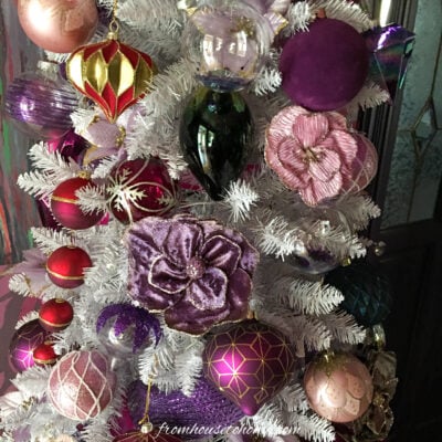 A close up of a white Christmas tree decorated with pink and purple ornaments.