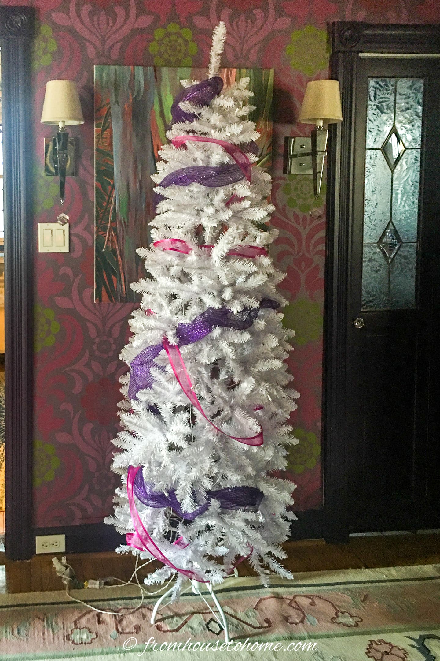A white Christmas tree decorated with pink and purple ribbon