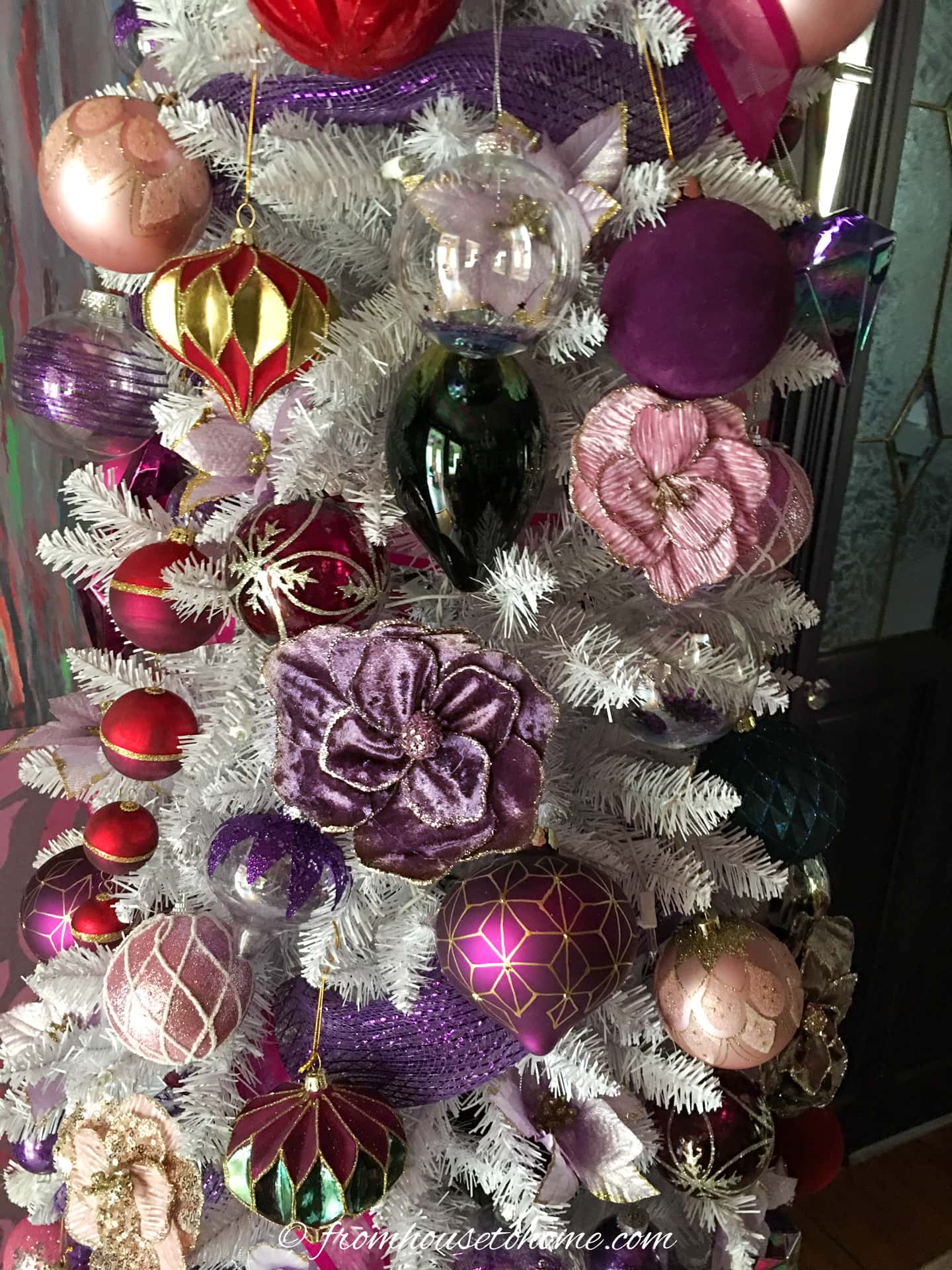 A closeup of a white Christmas tree decorated with purple and pink ball and flower ornaments