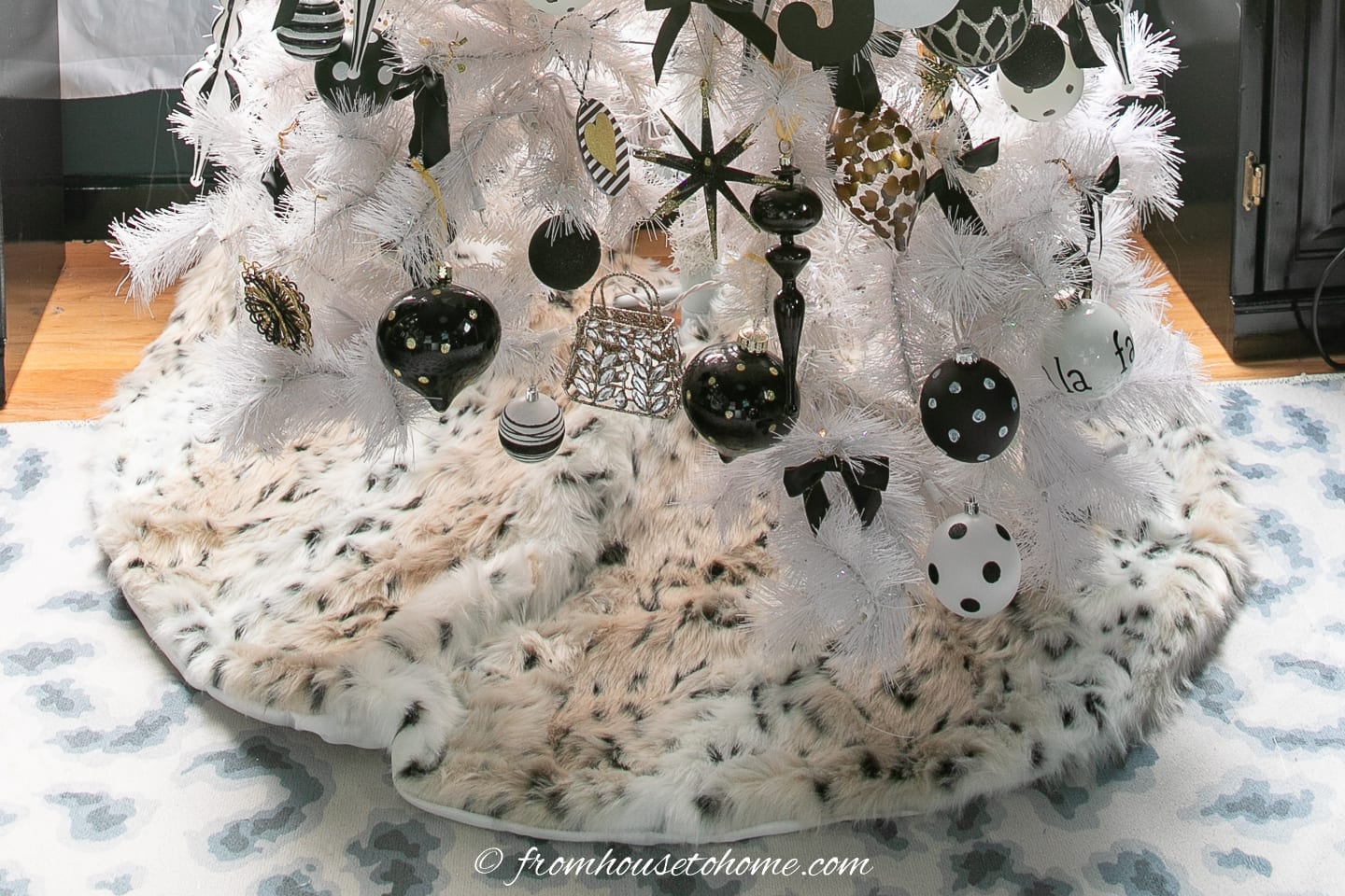 A leopard print tree skirt under a white Christmas tree with black ornaments