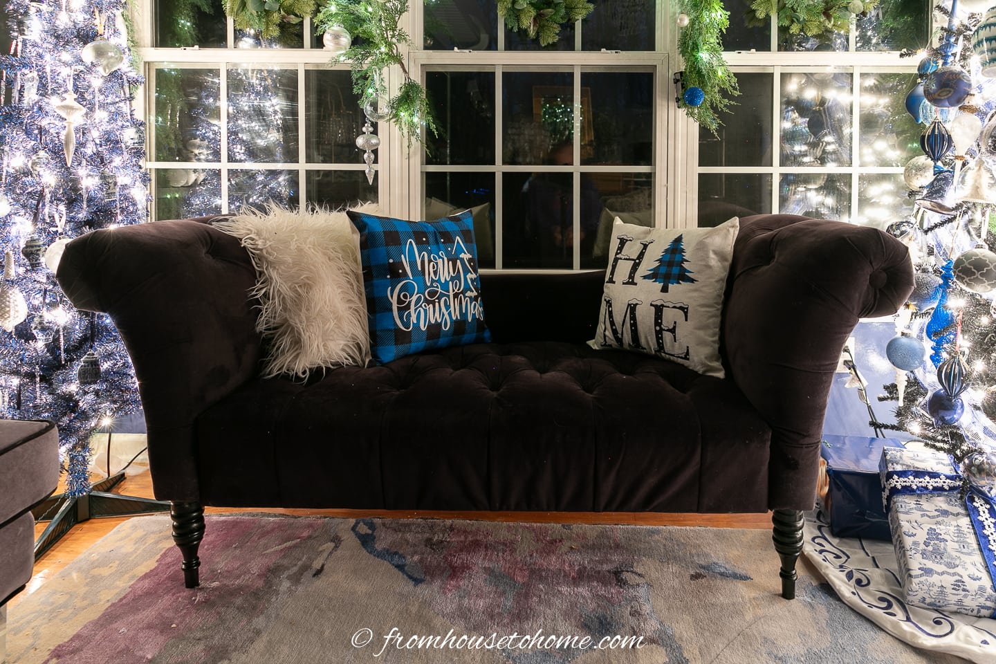 Black sofa with blue and white Christmas cushions between lighted Christmas trees