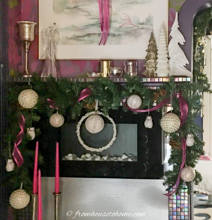 Fireplace mantel decorated with a garland with pink ribbon and white ornaments