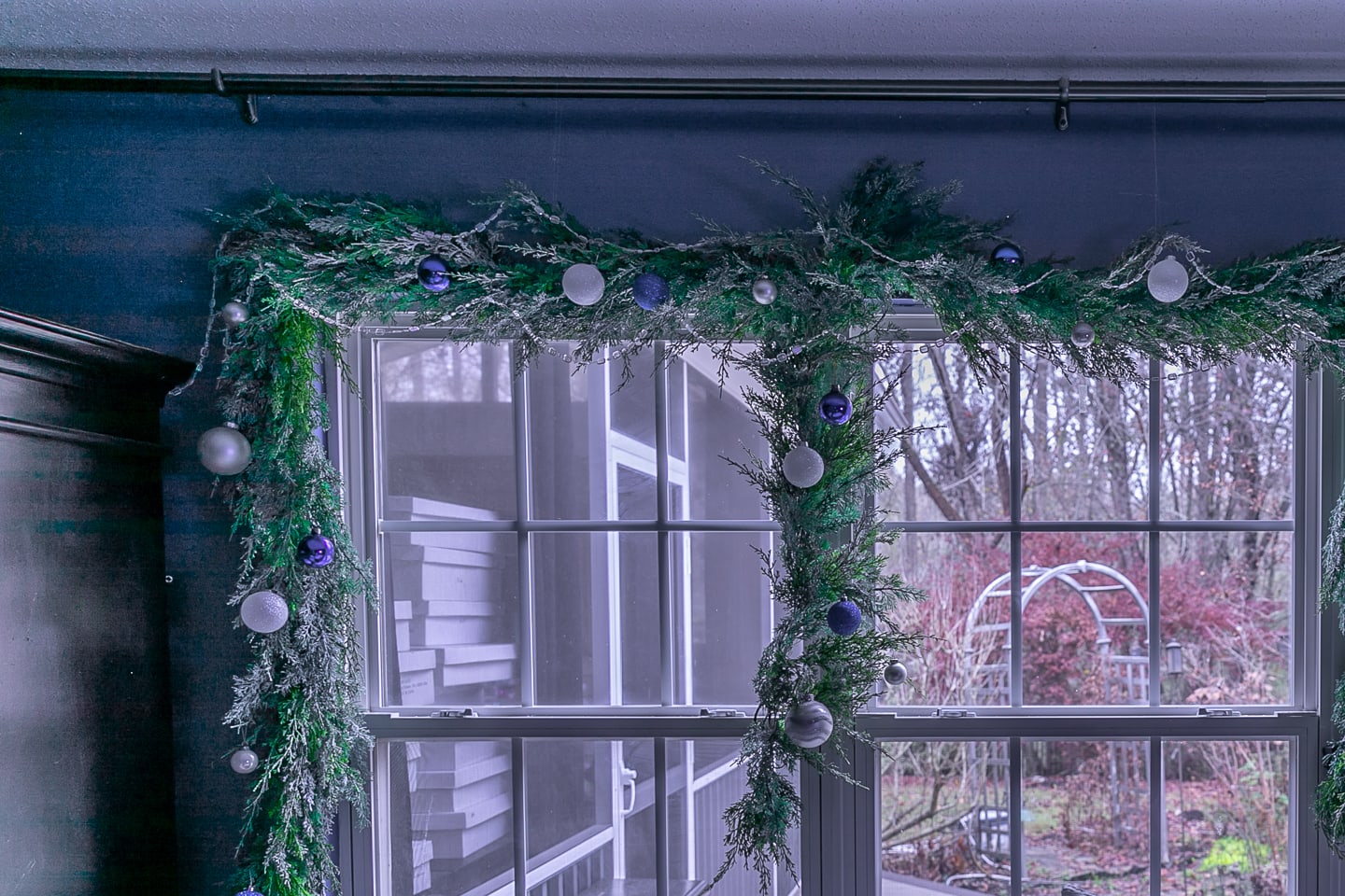 Ball Christmas ornaments and a string of glass beads hung from a garland over a window