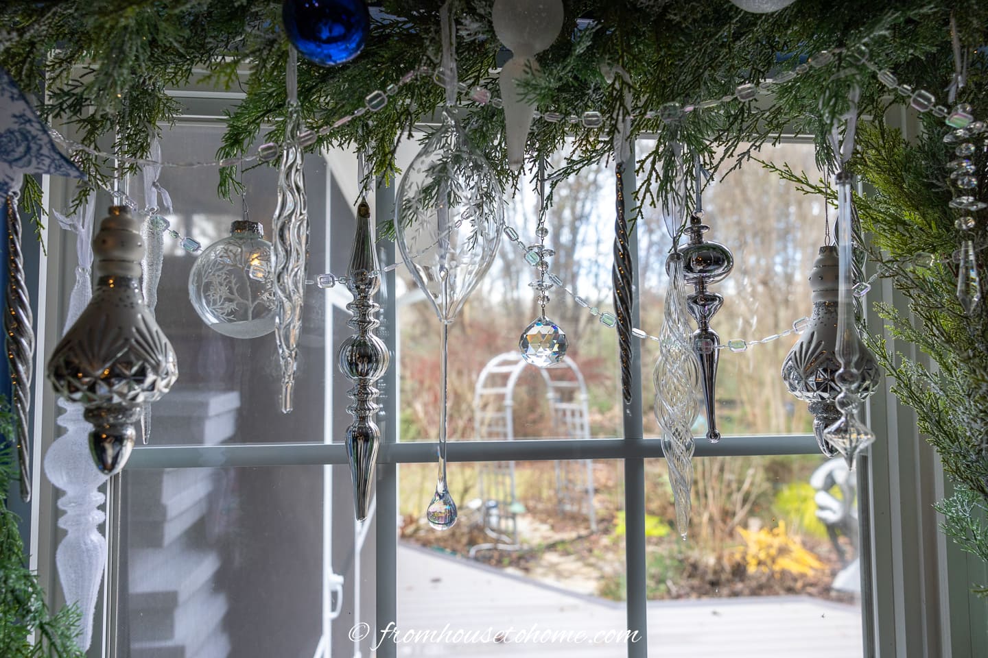 Clear glass, white and silver finial ornaments hung from a garland over a window