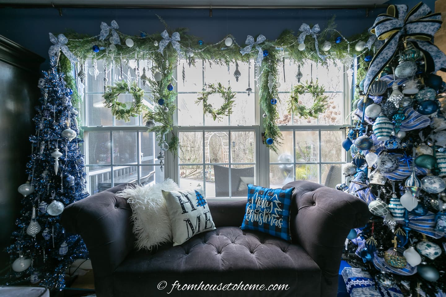 Decorated evergreen Christmas garland hung over a window with 3 wreaths