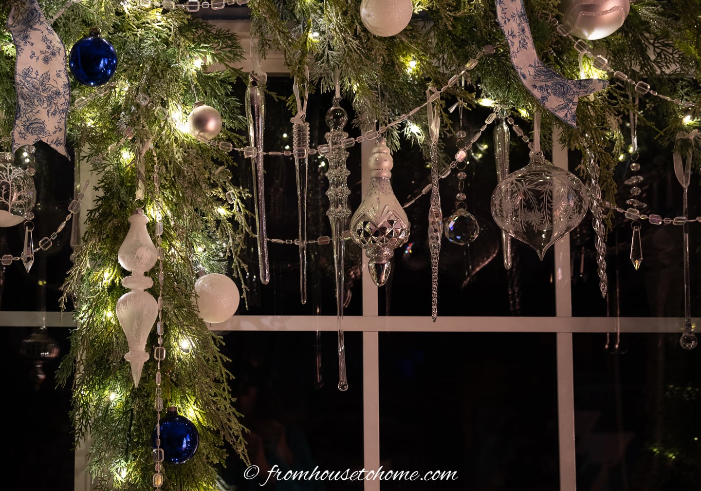 Clear glass ornaments hung over a garland with the lights on at night