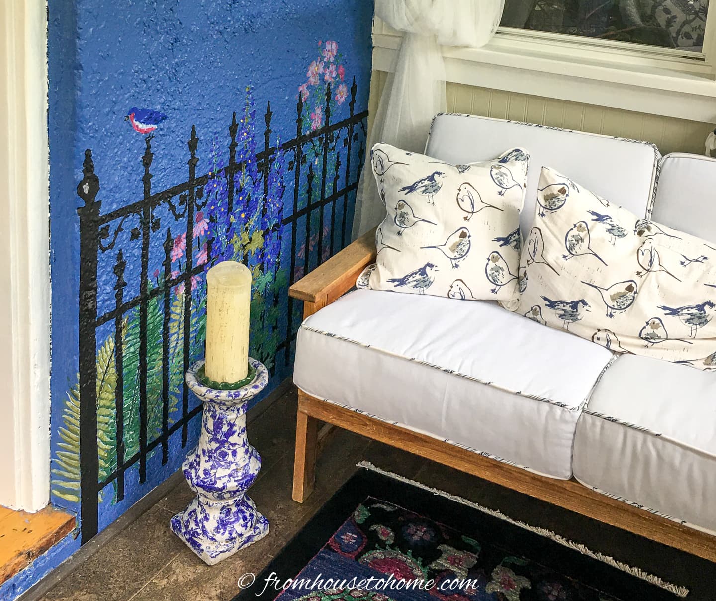 white outdoor sofa beside a blue and white candleholder and a garden fence stenciled on the wall