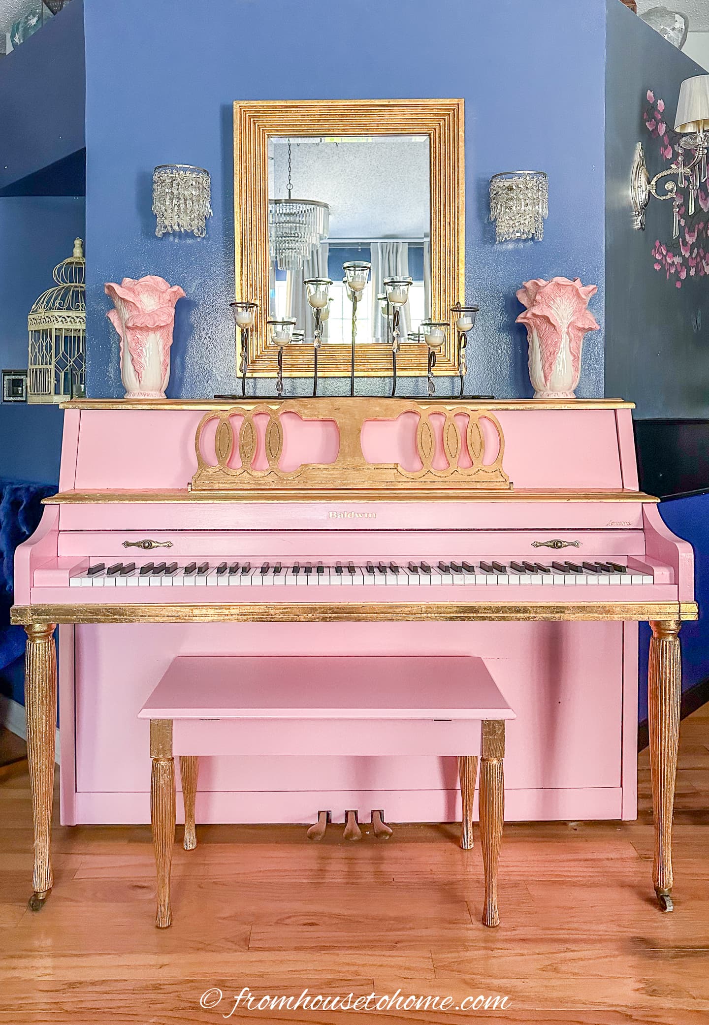 The pink piano with a gold leaf mirror over it and two pink and white vases on either end