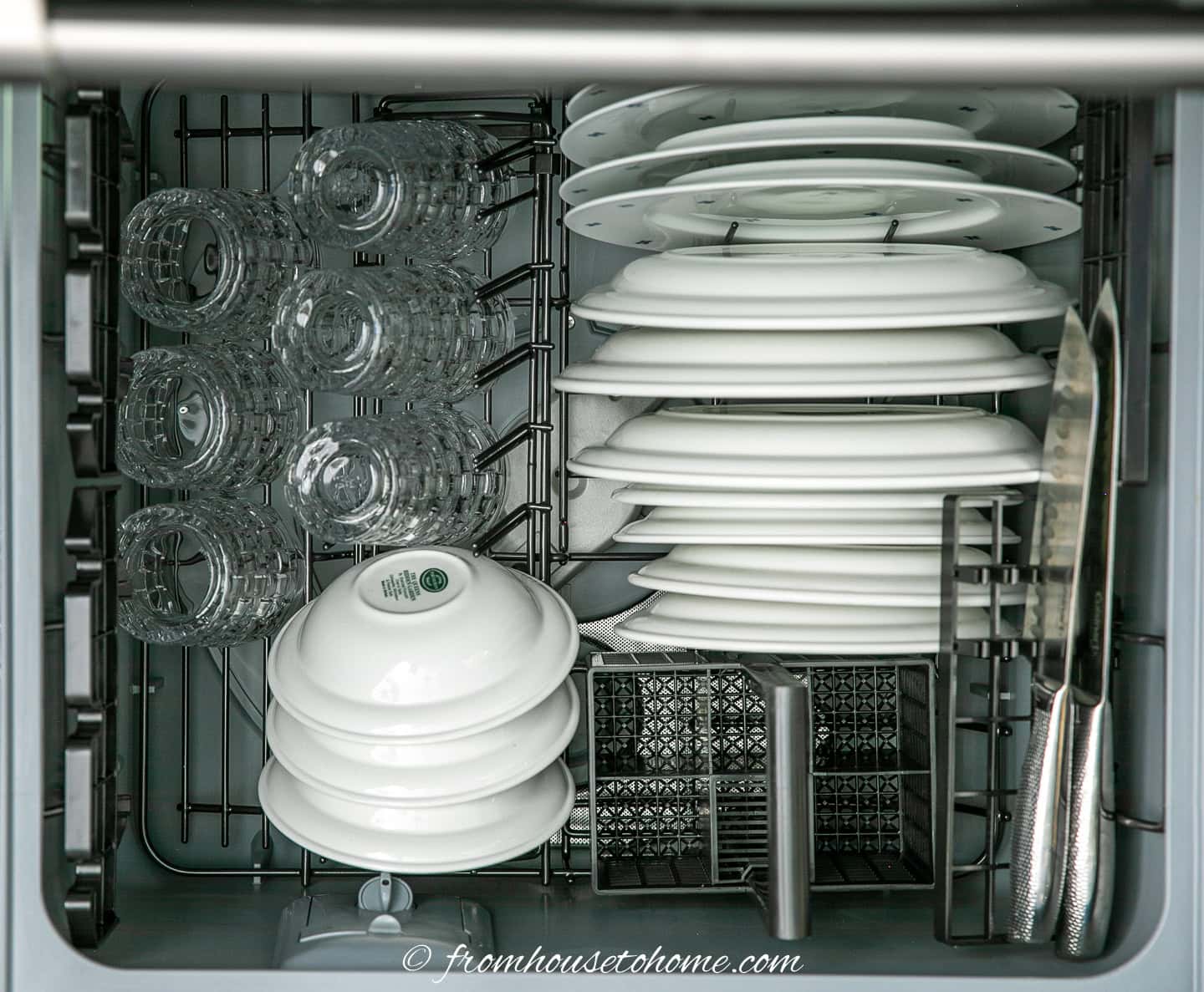 dishwasher drawer filled with lots of plates, some glasses, bowls and cutlery