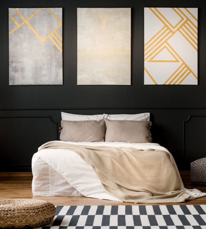 3 large paintings over a bed in a bedroom with black walls