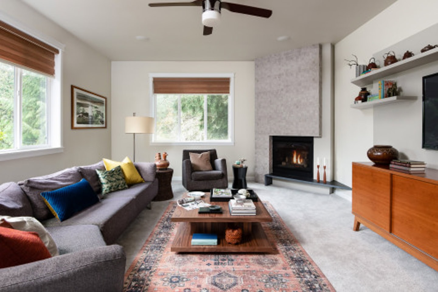 A long sofa, coffee table and area rung facing a long buffet beside an angled fireplace
